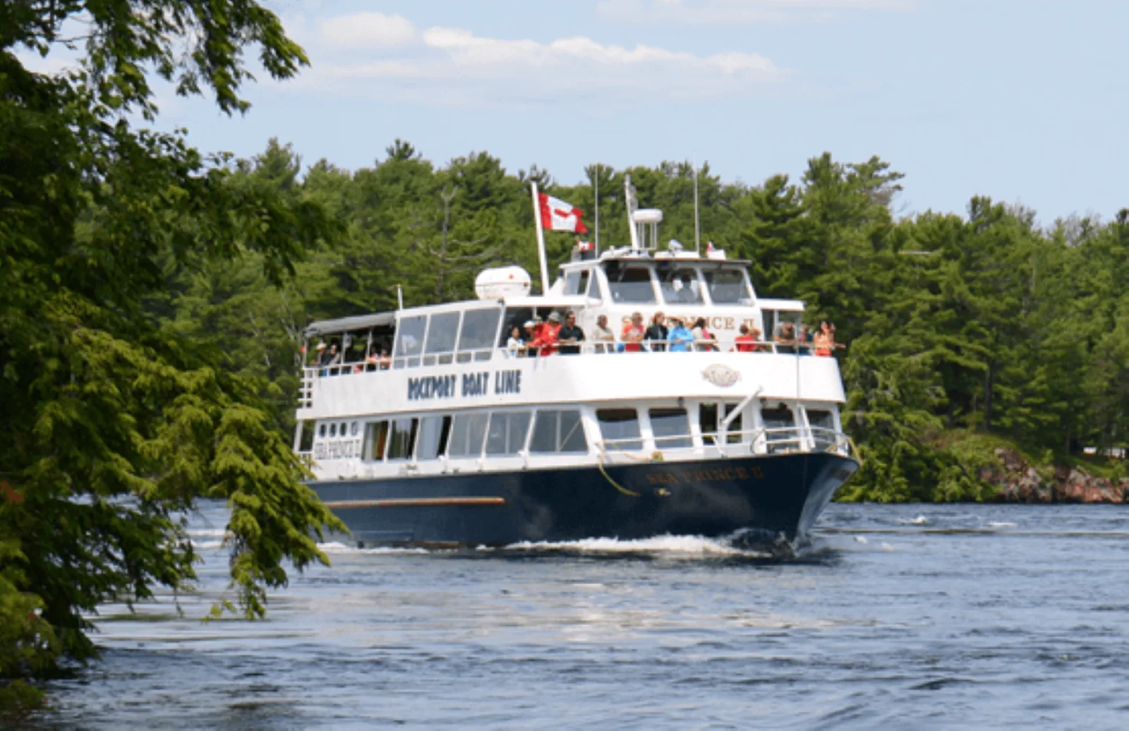 A Rockport Boat Line sightseeing vessel under way past the wooded granite shoreline of the 1000 Islands on the St. Lawrence River
